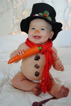 a baby in a snowman costume holding a carrot and wearing a black top hat