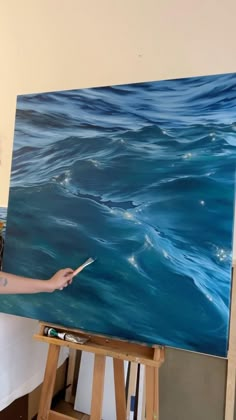 a woman is painting on an easel with blue water