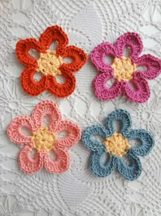 four crocheted flowers sitting on top of a white doily next to each other