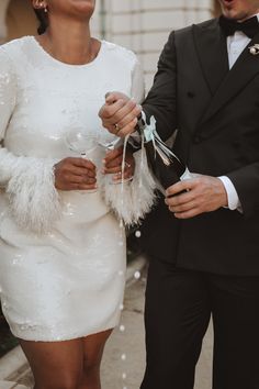 a man in a tuxedo and a woman in a white dress are walking down the street