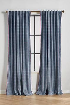 a blue and white curtain hanging in front of a window with wood flooring next to it