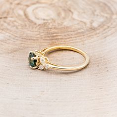 a gold ring with an emerald stone and three diamonds on it sitting on a wooden surface