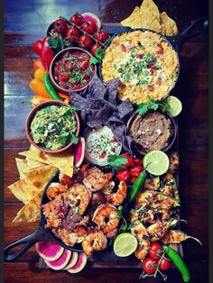 a platter filled with different types of food on top of a wooden table next to tortilla chips and guacamole