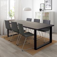 a dining room table with grey chairs in front of a white curtained window and wooden flooring