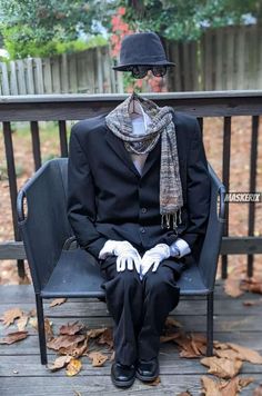 a man sitting on top of a bench wearing a suit and hat with gloves around his ankles