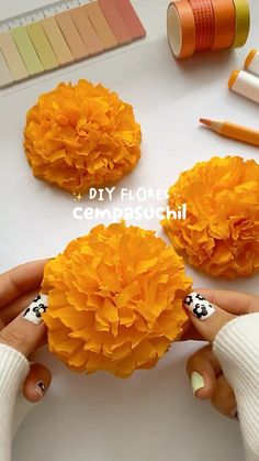 two orange flowers sitting on top of a white table next to markers and pencils