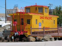 a yellow and red train caboose sitting on the side of a road next to rocks