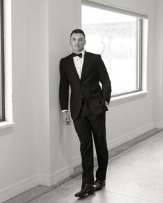 a man in a tuxedo leaning against a wall