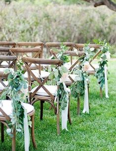 rows of wooden chairs decorated with greenery and ribbons for an outdoor ceremony in the grass