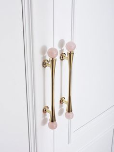 two gold handles on a white door with pink glass balls hanging from it's sides