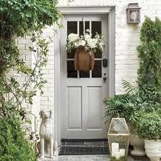 a white front door surrounded by greenery and potted plants with flowers in the basket