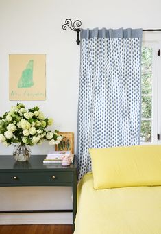 a bedroom with yellow and blue bedding and flowers on the nightstand next to the window