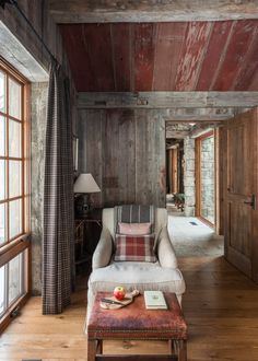 a living room with wood paneling and plaid pillows on the couch, along with an ottoman