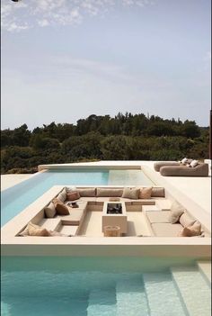 an outdoor living area with couches and tables next to a swimming pool in front of trees