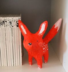 a red rabbit figurine sitting next to a stack of books on a shelf