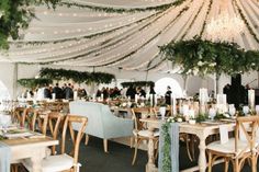 a large tent with tables and chairs covered in greenery, candles and white linens