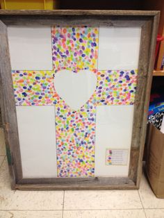 a cross made out of colored dots is displayed in a wooden frame on the floor