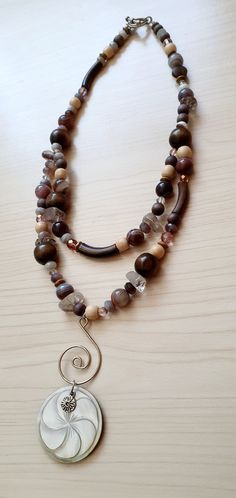 "Fibonacci Multi Stone Agate Bohemian Necklace by GlamRox. Fibonacci Shell Pendant. Multi Gemstone Botswana Agate Wood Necklace Boho Stunning Double Strand Bib Drop Long Necklace comprise of genuine Botswana Agate, Wood, Rutilated Quartz and Czech Glass featuring a stunning drop of a Fibonacci Spiral and Carved Mother of Pearl Pendant! Truly beautiful on and so unique. Hand made and designed by yours truly, GlamRox Necklace measures: 21 inches long Pendant Section: 3.5 inches long Don't miss out Handmade Brown Double Strand Jewelry, Brown Spiral Necklace For Gifts, Handmade Spiral Brown Jewelry, Unique Brown Spiral Jewelry, Bohemian Spiral Jewelry For Healing, Fibonacci Shell, Fibonacci Spiral, Mother Of Pearl Pendant, Botswana Agate