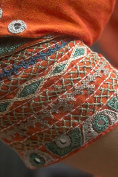 a close up of a person's arm wearing an orange shirt and patterned shorts