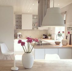 a white vase filled with flowers sitting on top of a wooden table in a kitchen