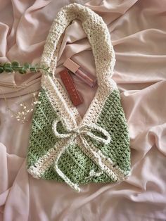 a crocheted green and white purse laying on top of a pink bed sheet