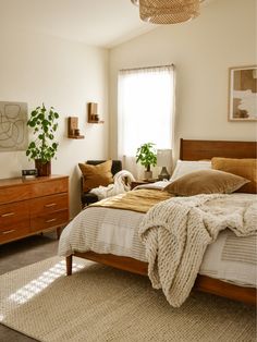 a bed room with a neatly made bed and two plants on the side of the bed