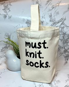 a tote bag with the words must knit socks printed on it next to a succulent