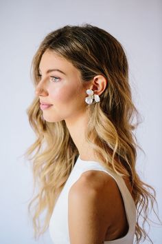 a woman with long blonde hair wearing white dress and flower earring on her left ear