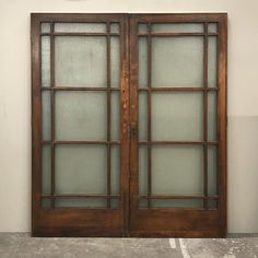 two wooden doors with frosted glass on the top and bottom, in front of a white wall