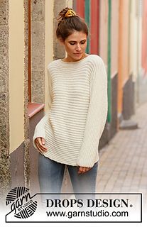 a woman standing in front of a building wearing a white sweater and jeans with a ponytail