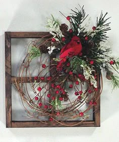 a red bird sitting on top of a wooden frame filled with berries and greenery