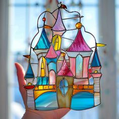 a hand holding up a stained glass castle ornament