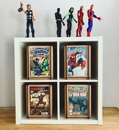 some action figures are sitting on top of a book shelf in front of a wall