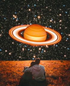 two people are sitting in the grass looking at an image of saturn and its rings