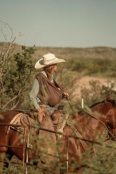 a woman riding on the back of a brown horse next to a wooden fence in a field