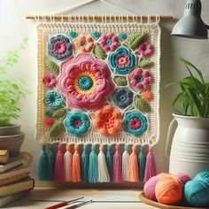 a crocheted wall hanging with flowers and tassels on it next to some books