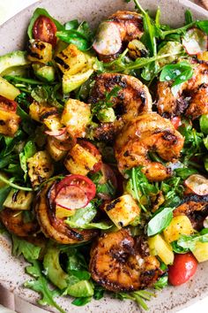 a salad with shrimp, avocado and tomatoes in a bowl on a table