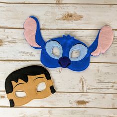 two masks are sitting on a white wooden surface, one is blue and the other has pink ears