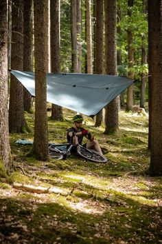 a man sitting in the woods under a tarp with his bike parked next to him