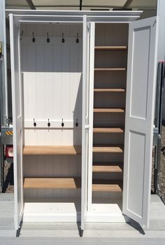 an open white storage cabinet with shelves and hooks on the doors, in front of a trailer