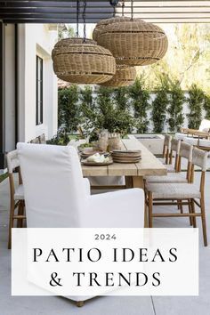 an outdoor dining area with white chairs and wicker hanging from the ceiling, surrounded by greenery