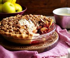 a close up of a pie on a plate near bowls of fruit and a bowl of yogurt