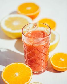 an orange drink with ice sits on a table next to sliced oranges and slices of lemon