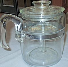 a clear glass tea pot with a lid on a white table cloth covered tablecloth