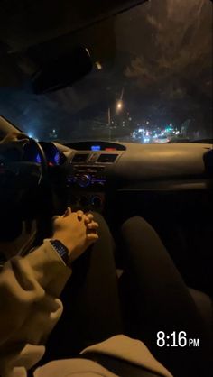 the man is driving in his car at night with city lights behind him and onlookers