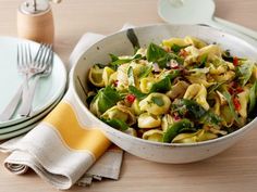 a white bowl filled with pasta and vegetables on top of a table next to plates