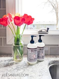 red tulips in a vase next to two bottles of hand soap on a kitchen counter