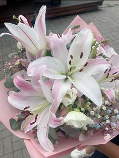 pink and white flowers are in a bouquet on the ground with someone's hand