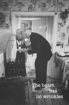 an old man and woman standing next to each other in front of a window with the words, the heart has no wrinkles