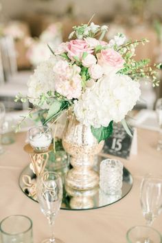 a vase filled with white and pink flowers on top of a table next to wine glasses